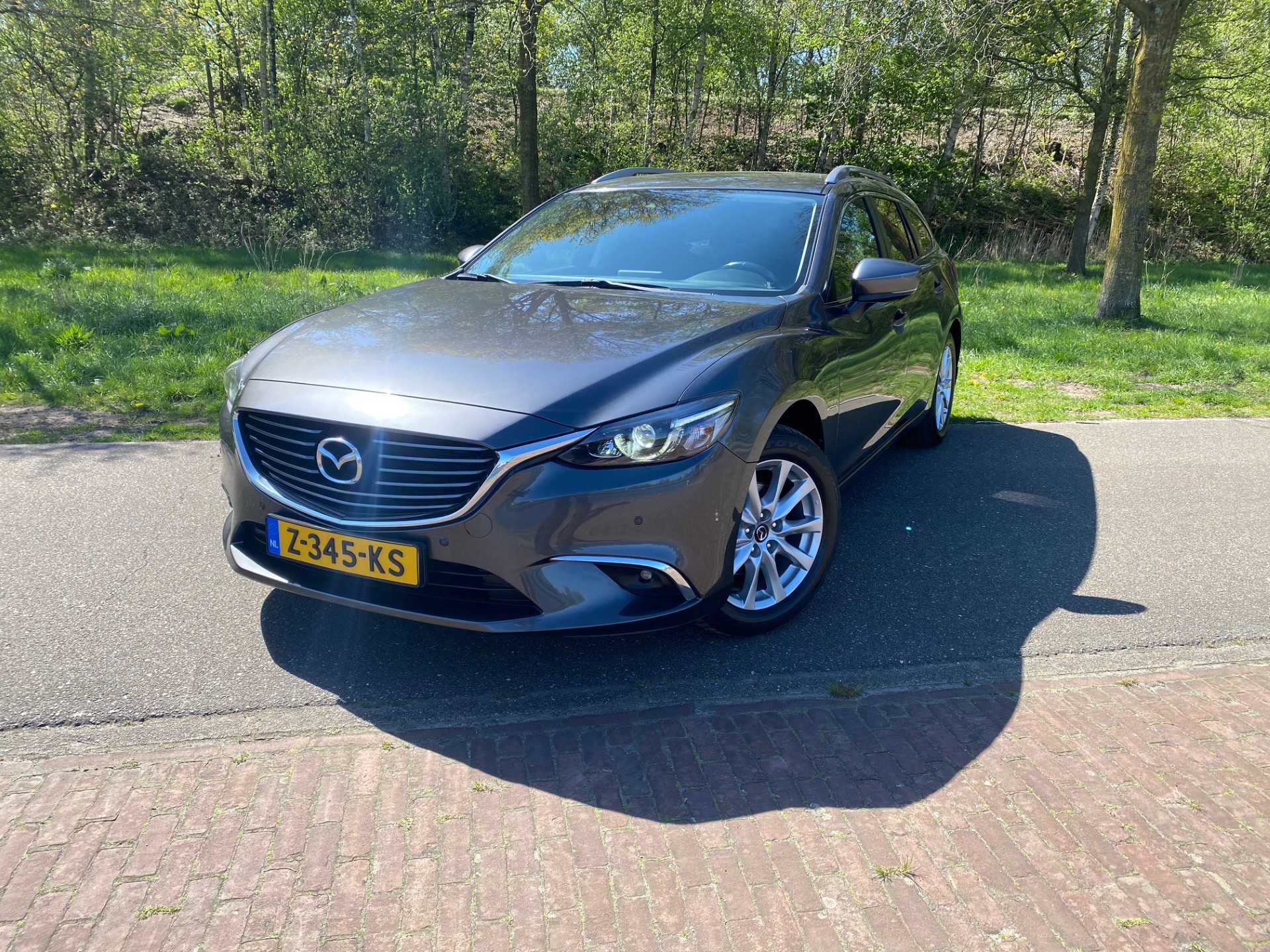 Een Mazda 6 Sportbreak op de weg langs de bomen, een van onze occasions